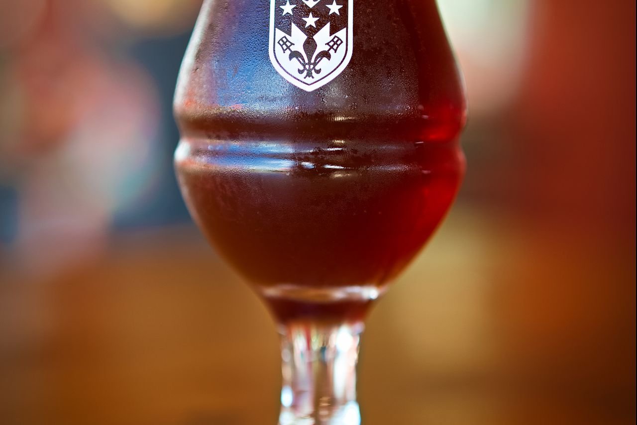 A crystal-clear golden double IPA in an elegant tulip glass held against soft light, showing the deep amber color