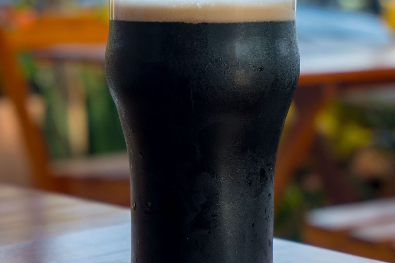 A deep, dark barrel-aged stout in a snifter glass held against natural light showing ruby-brown color and thick head