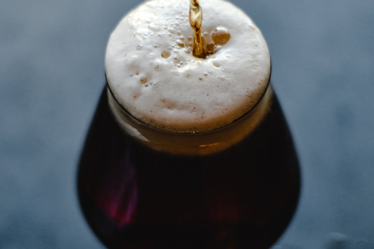 A bottle of saison being poured into a tall tulip glass, showing the hazy golden color and large rocky foam head