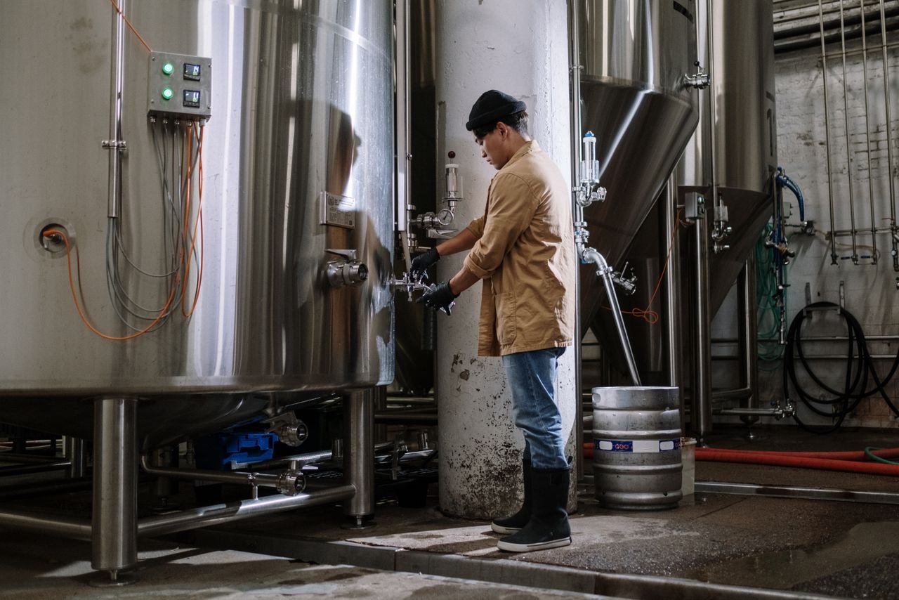 Brewmaster monitoring beer production in a modern craft brewery with large stainless tanks