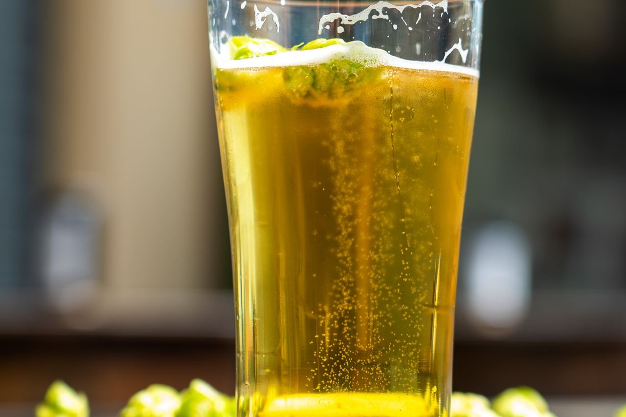 Close-up of fresh green hop cones piled on a wooden surface next to a glass of pale ale