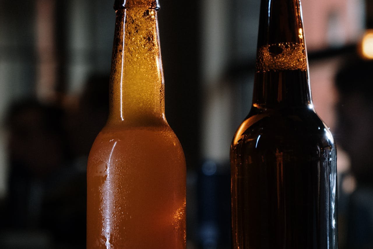 Row of capped homebrew bottles with handwritten labels resting on a wooden shelf