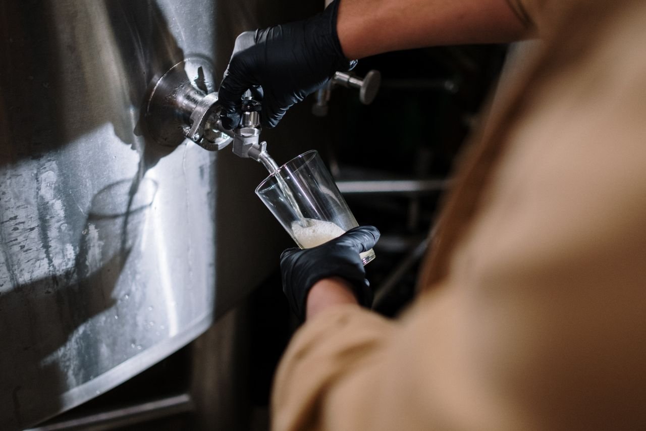 Brewer pouring golden wort from a large tank into a fermenter during a brew day