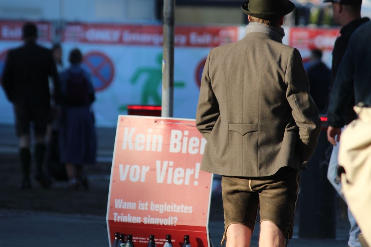 Festival attendee in Bavarian hat holding a beer stein next to a wooden sign