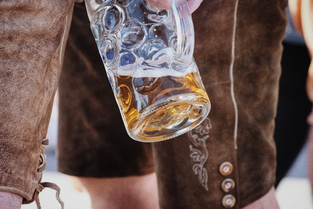 Person in traditional lederhosen holding a full beer stein at an outdoor festival