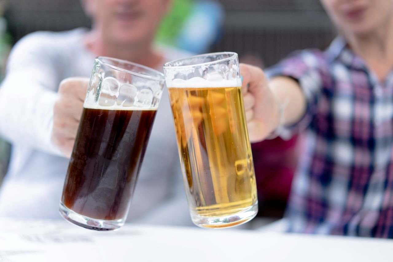 Pair of glass beer steins — one golden lager, one dark — side by side on a wooden bar