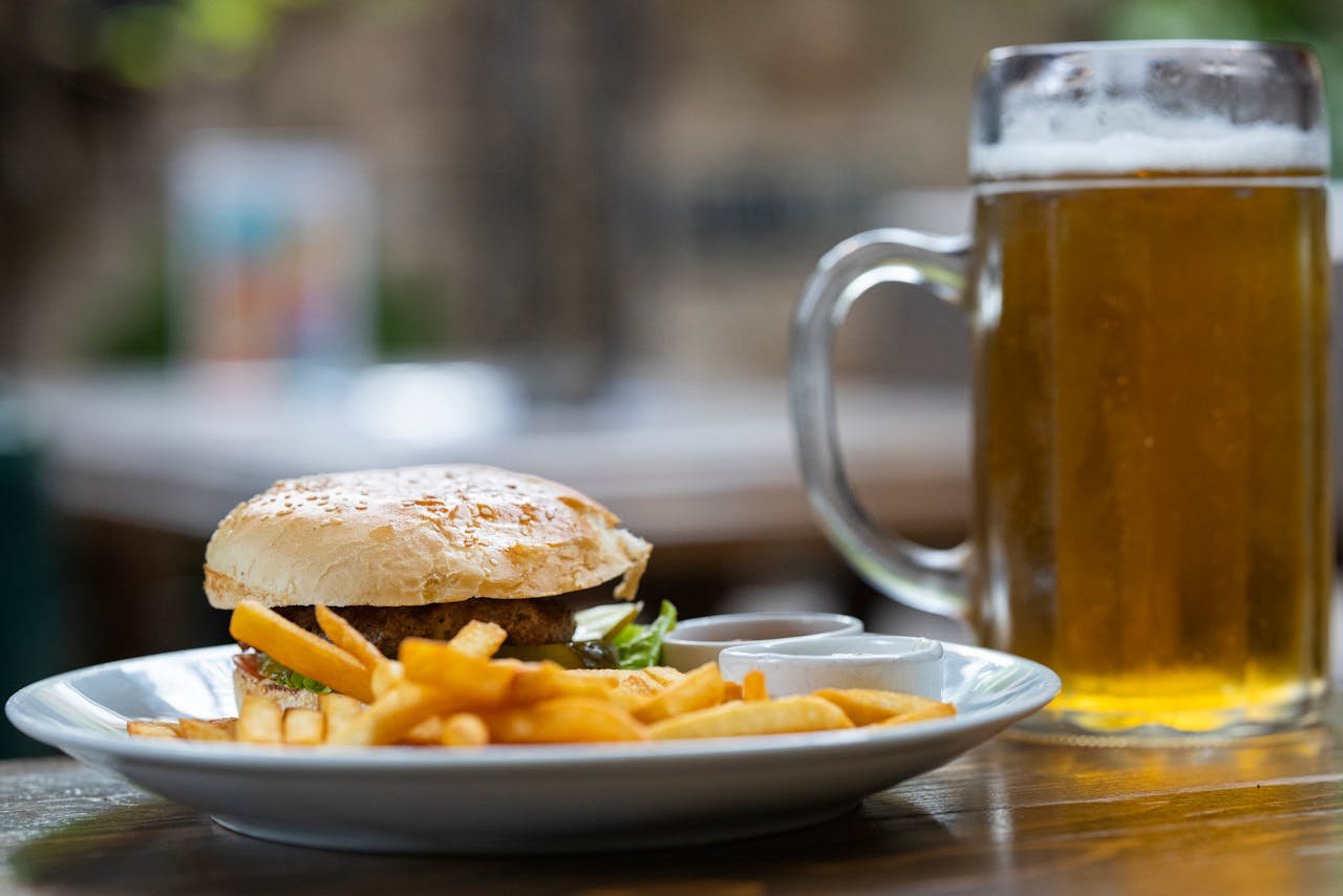 A cold pint of beer beside a burger and fries at a casual restaurant