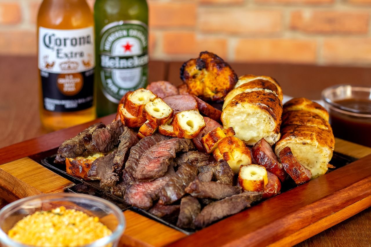Grilled meat on a platter alongside a glass of amber beer outdoors