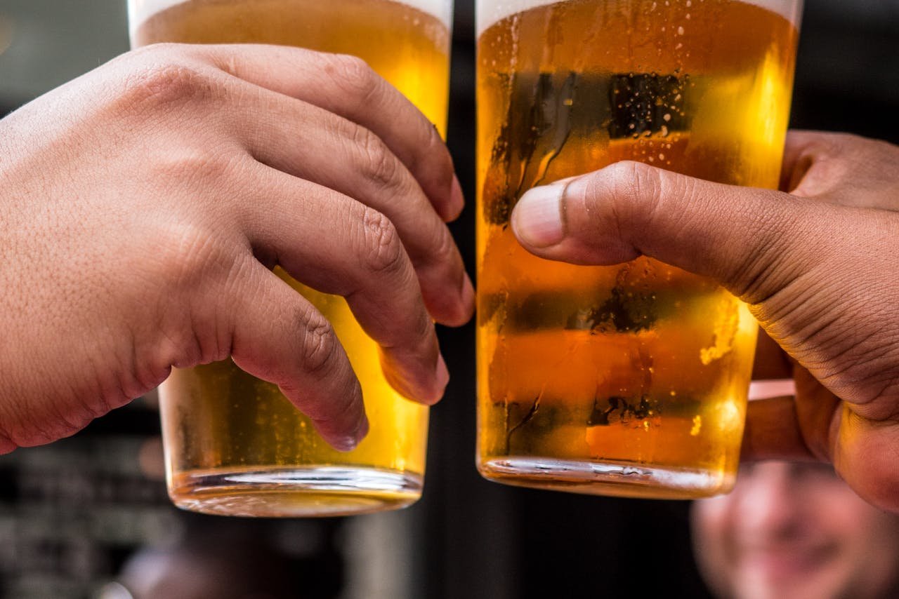 Two hands holding pints of beer over a table set with food